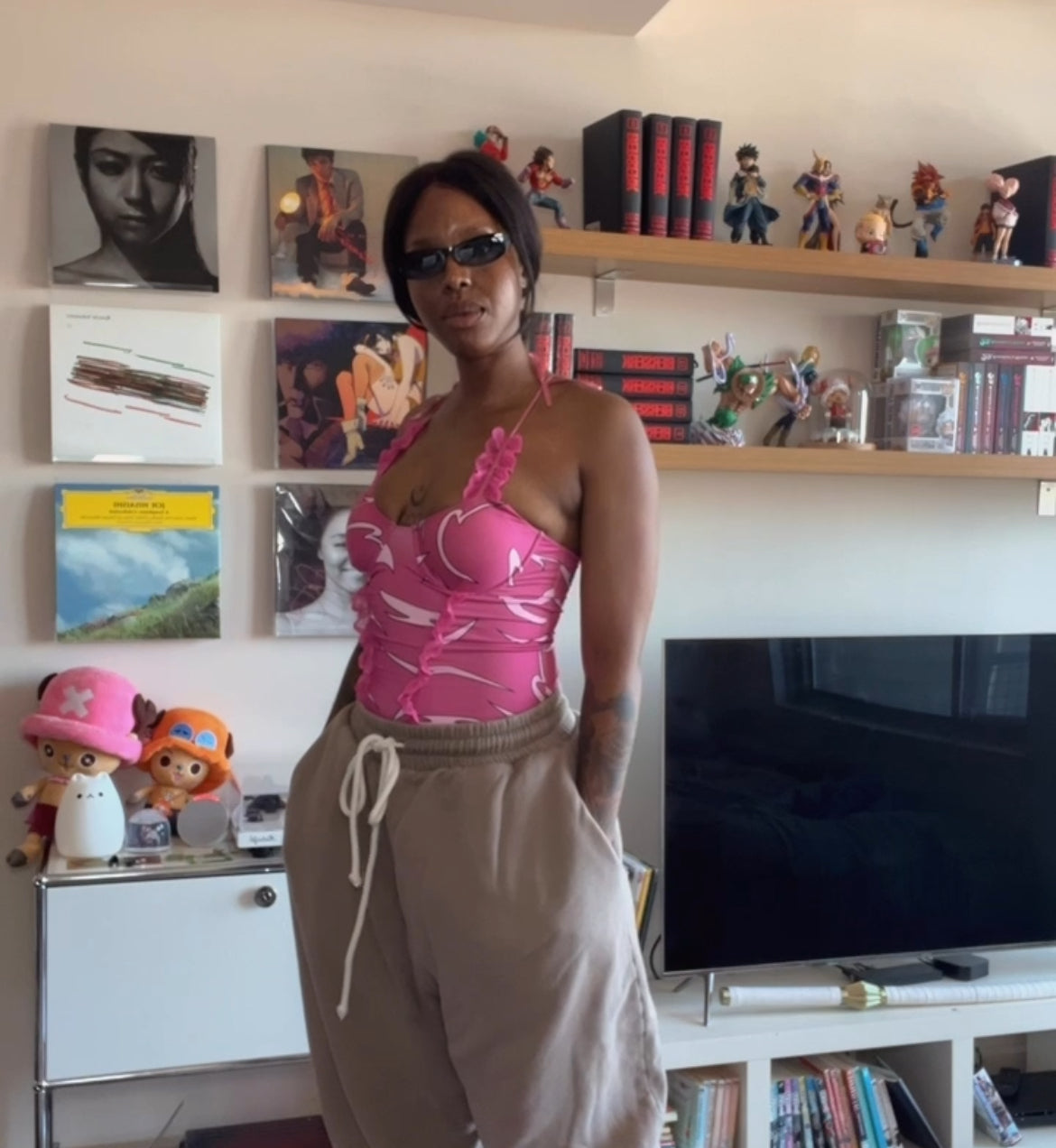 Woman in a pink top and beige pants standing in a room with shelves and books.